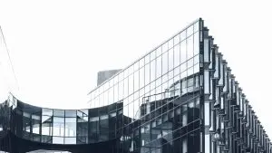 A modern glass building with reflective windows and a curved architectural design on its facade against a white sky background.