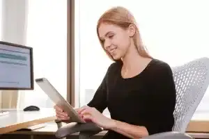 A woman sitting in an office chair using a tablet computer.