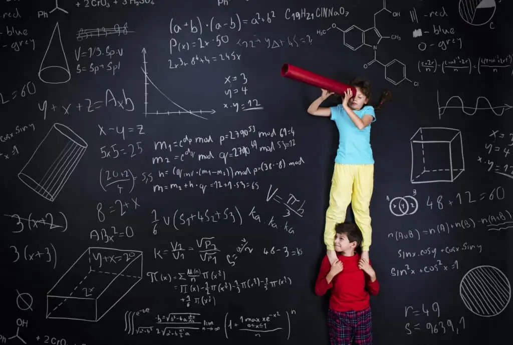 Two kids' financial literacy while standing in front of a blackboard with formulas written on it.