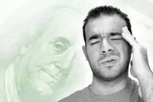 A man appears to be stressed or troubled with the image of a US dollar bill overlayed in the background, symbolizing the genesis of money troubles.