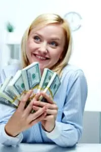 Woman holding a stack of cash with a pleased expression, clearly enjoying the success of her finances.