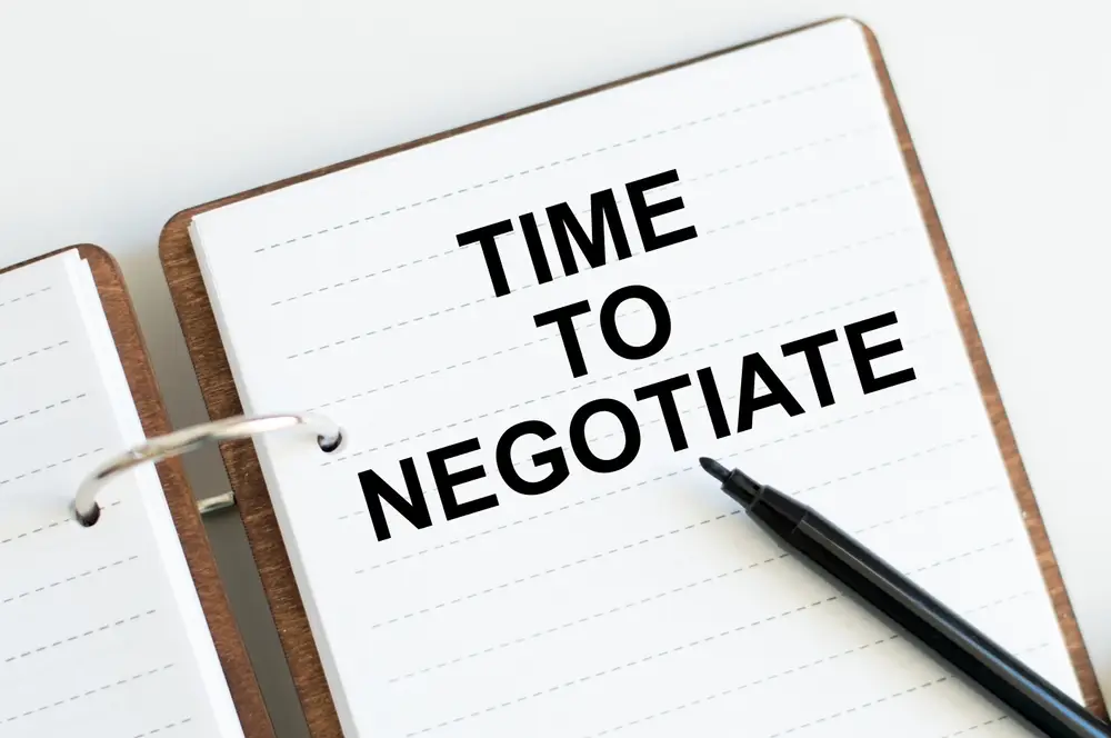 A notebook with the words "TIME TO NEGOTIATE" printed in bold, black letters, accompanied by a black pen—perfect for strategizing how to negotiate better rates on loans.