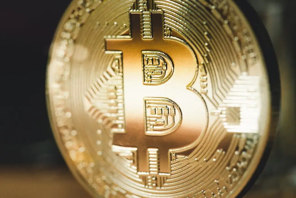 Close-up of a golden Bitcoin coin, displaying the Bitcoin symbol and intricate design details. The metallic surface reflects light, emphasizing the coin's detailed engravings, emblematic of our shift towards a cashless world powered by digital currencies.