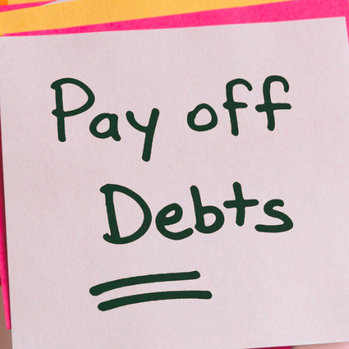 A sticky note with the phrase "Pay off Debts" written on it in large, clear handwriting, possibly suggesting the need for Debt Reduction Services.