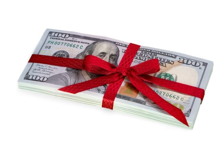 A festive stack of 100-dollar bills, tied with a vibrant red ribbon, makes the perfect gift to generate some holiday cheer.