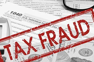 A stack of U.S. tax forms emblazoned with "Understanding Tax Fraud" in red letters, featuring dollar bills and a calculator, serves as a crucial reminder to protect from risks associated with financial missteps.
