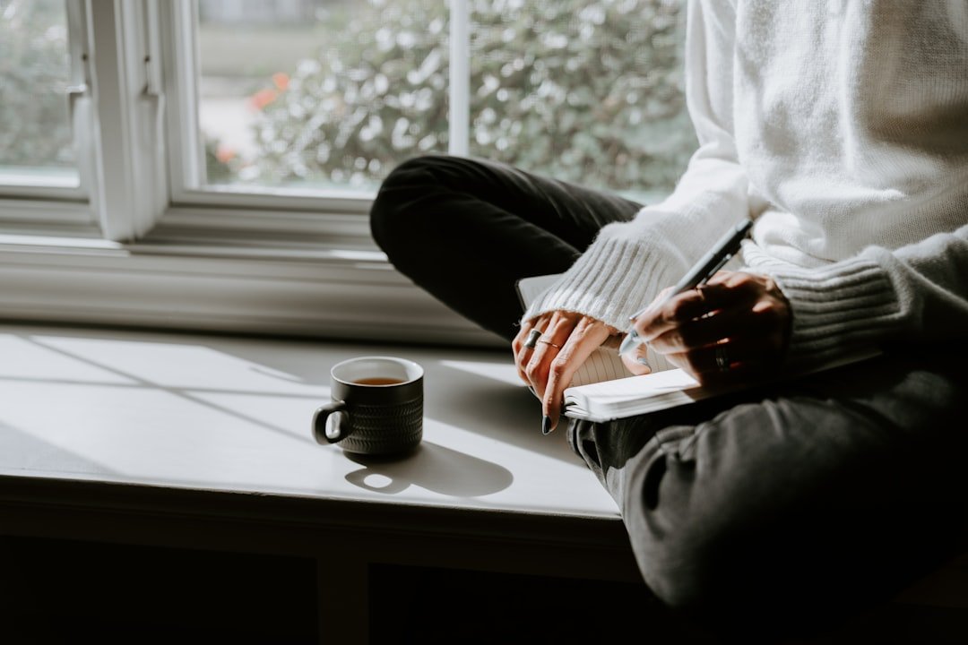 Underconsumption-core: A Fresh Money Mindset 1 A person sits quietly by a window with a cup of coffee, embodying the calm, intentional simplicity at the heart of underconsumption-core.